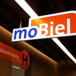 Innen: 3D-Leuchtlogo „moBiel“, Flachmaterial Vollacryl 30 mm, in Form geschnitten. Belegt mit transluzenter 3M-Folie in blau / orange nach CI. Ausleuchtung durch LED. Montage mittels filigraner Halterung an der Decke, freihängend. moBiel - Adventsbahn